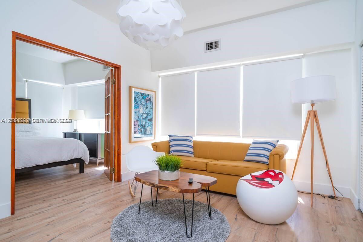A living room with a yellow sofa, wood coffee table, and an adjacent bedroom — 227 1st St # 7, Miami Beach FL 33139, MIAMI BEACH, FL