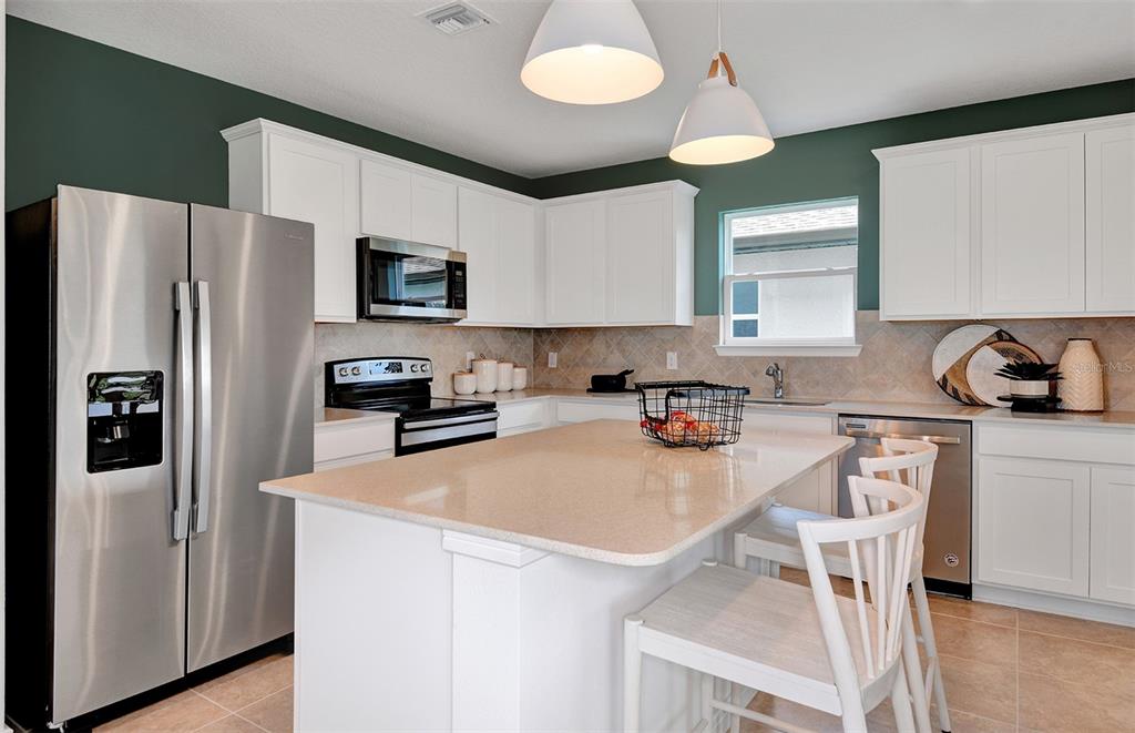 A kitchen features white cabinets, stainless steel appliances, a center island, and dark green walls — 10414 HIDDEN BANKS GLEN, PARRISH, FL