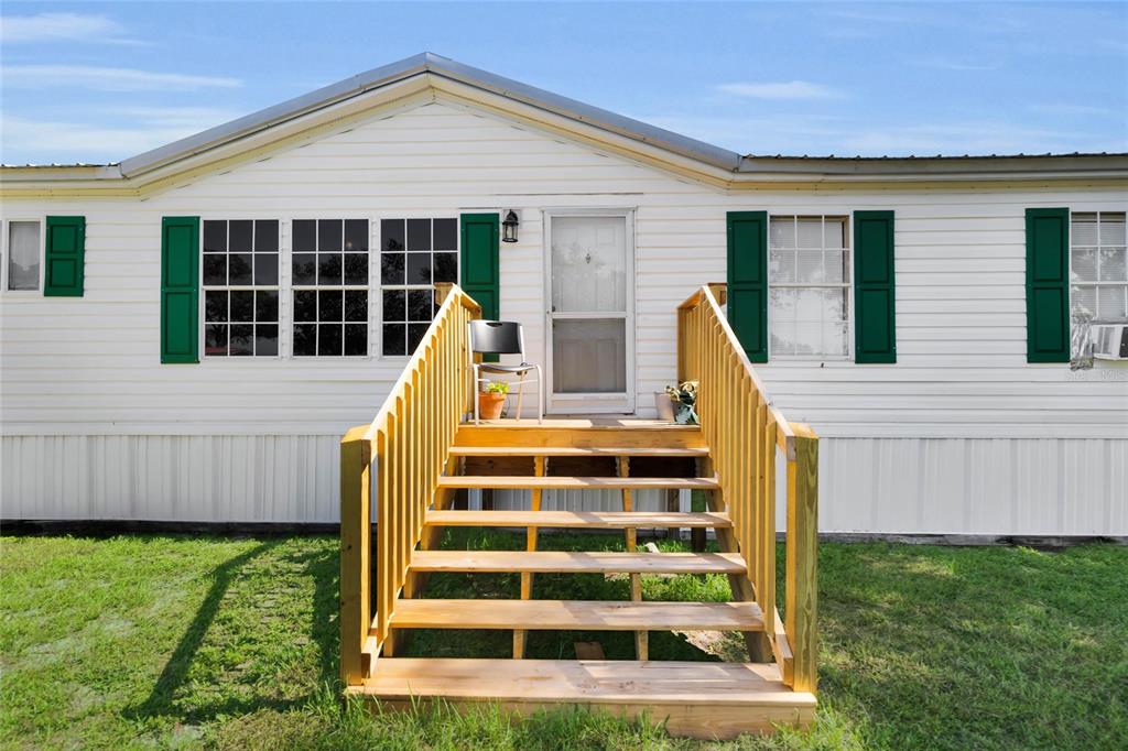 A white mobile home with green shutters and a wooden staircase leading to the entrance — 1725 MARKER ROAD, POLK CITY, FL