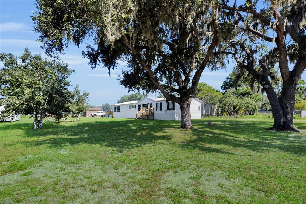 A white manufactured home sits on a grassy lot shaded by large, moss-covered oak trees — 1725 MARKER ROAD, POLK CITY, FL