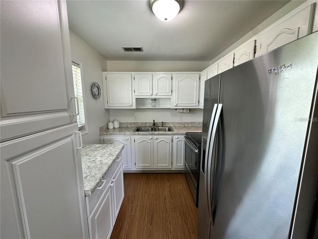 A kitchen features white cabinets, granite-look countertops, stainless steel appliances, and wood-look flooring — 11725 BOYNTON LANE UNIT 71A, NEW PORT RICHEY, FL