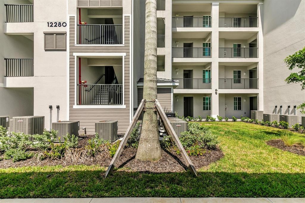 A multi-story apartment building exterior features balconies, air conditioning units, and a central palm tree — 12280 WELLEN GOLF STREET UNIT 203, VENICE, FL