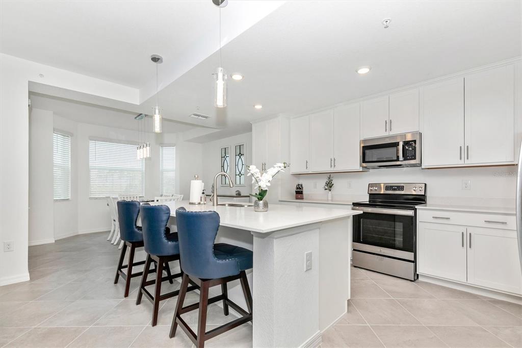 A kitchen with white cabinets, stainless steel appliances, and a central island with blue stools — 12280 WELLEN GOLF STREET UNIT 203, VENICE, FL