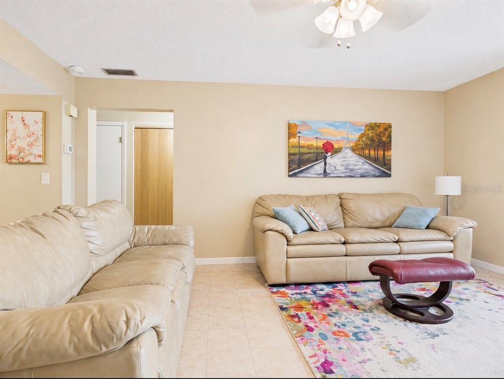 A living room features two beige leather sofas, a colorful area rug, and wall art — 2450 PELICAN COURT UNIT 202Q, CLEARWATER, FL
