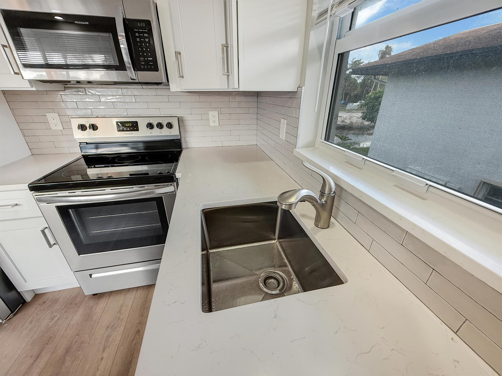 A kitchen features white cabinets, quartz countertops, a stainless steel sink, and a glass window — 13586 Sabal Palm Court # D, Delray Beach FL 33484, DELRAY BEACH, FL