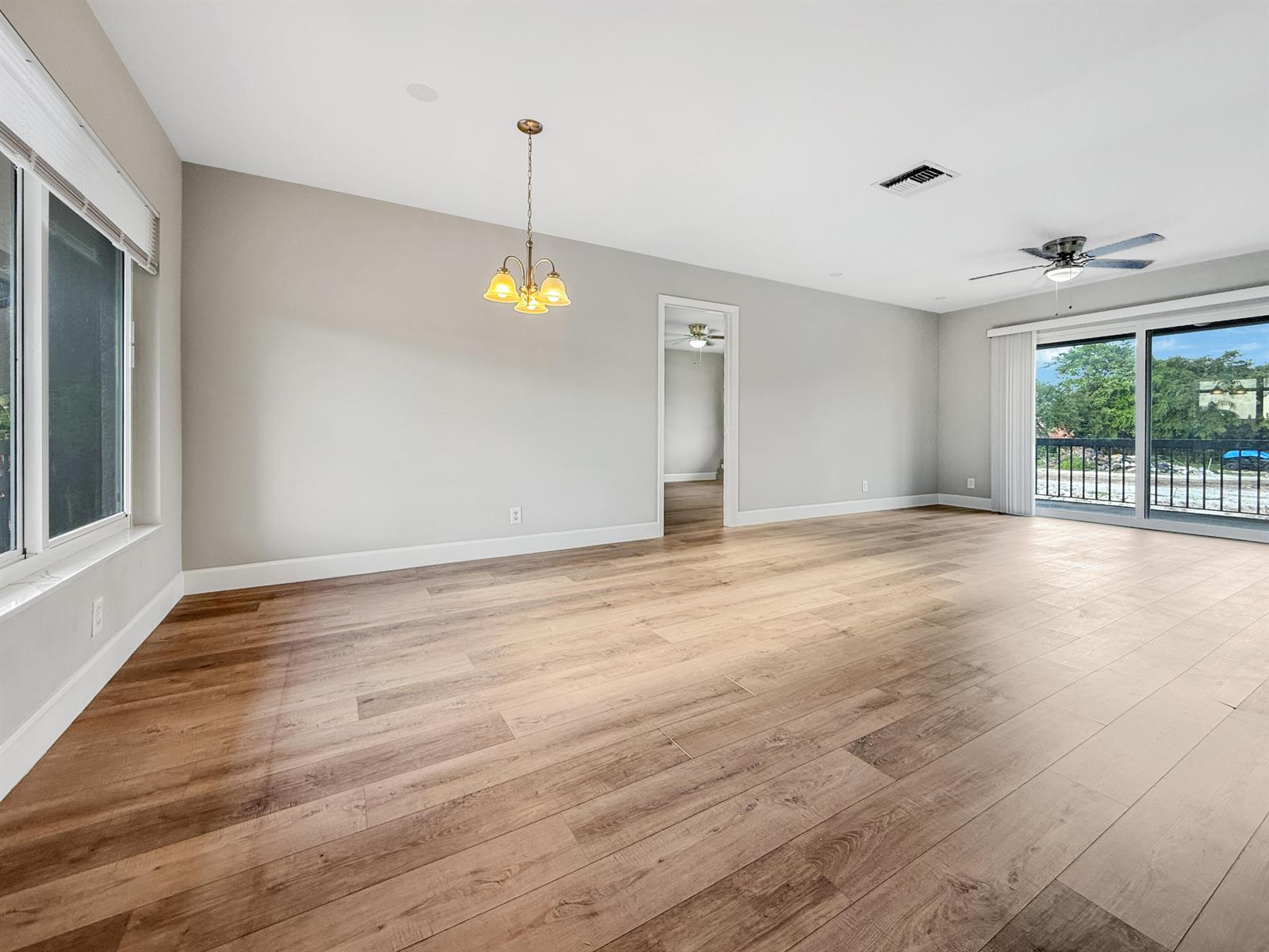 An empty living room features light gray walls, wood-look flooring, a chandelier, and sliding glass doors — 13586 Sabal Palm Court # D, Delray Beach FL 33484, DELRAY BEACH, FL