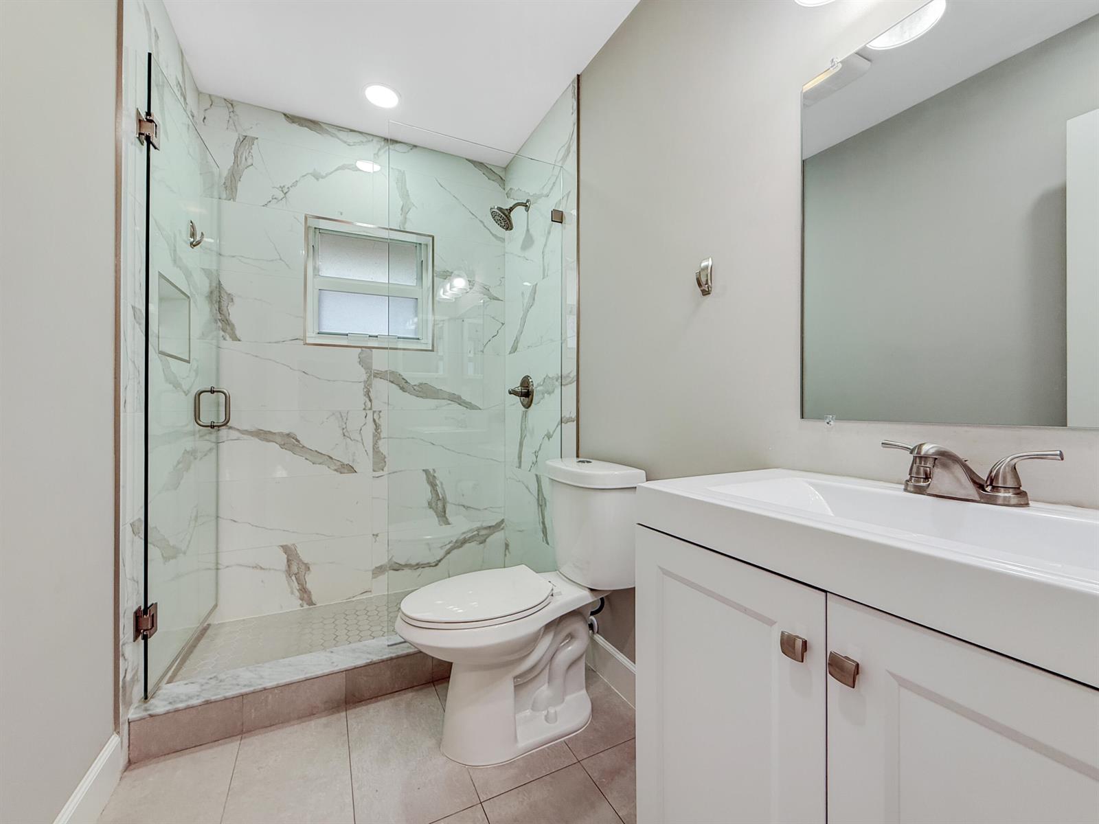A bathroom features a glass-enclosed marble-tiled shower, a white toilet, and a vanity with sink — 13586 Sabal Palm Court # D, Delray Beach FL 33484, DELRAY BEACH, FL