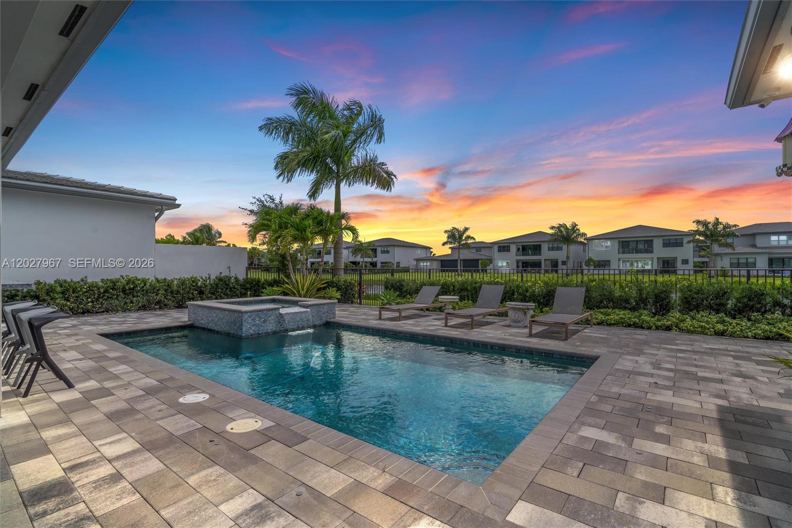 A backyard swimming pool with a spa and lounge chairs sits under a sunset sky — 20108 Castle Stuart Ave, Boca Raton FL 33434, BOCA RATON, FL
