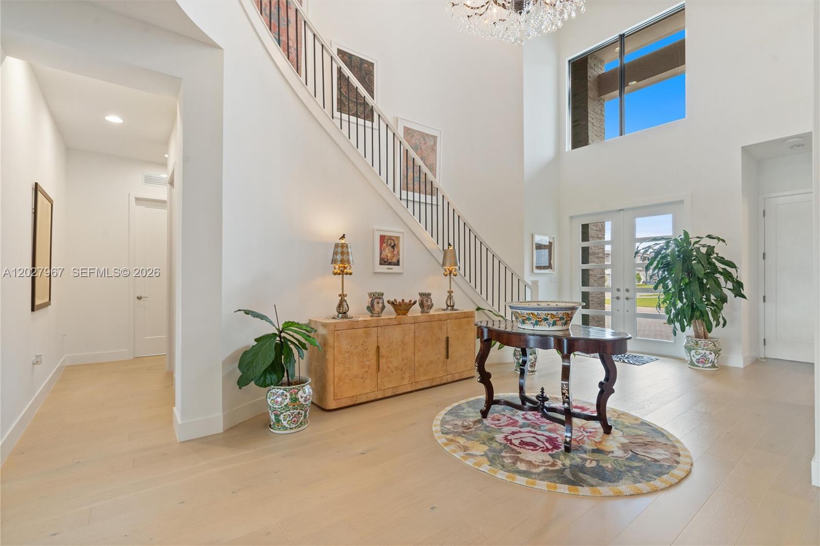 A bright, high-ceilinged foyer features a staircase, a wooden console table, and a floral rug — 20108 Castle Stuart Ave, Boca Raton FL 33434, BOCA RATON, FL