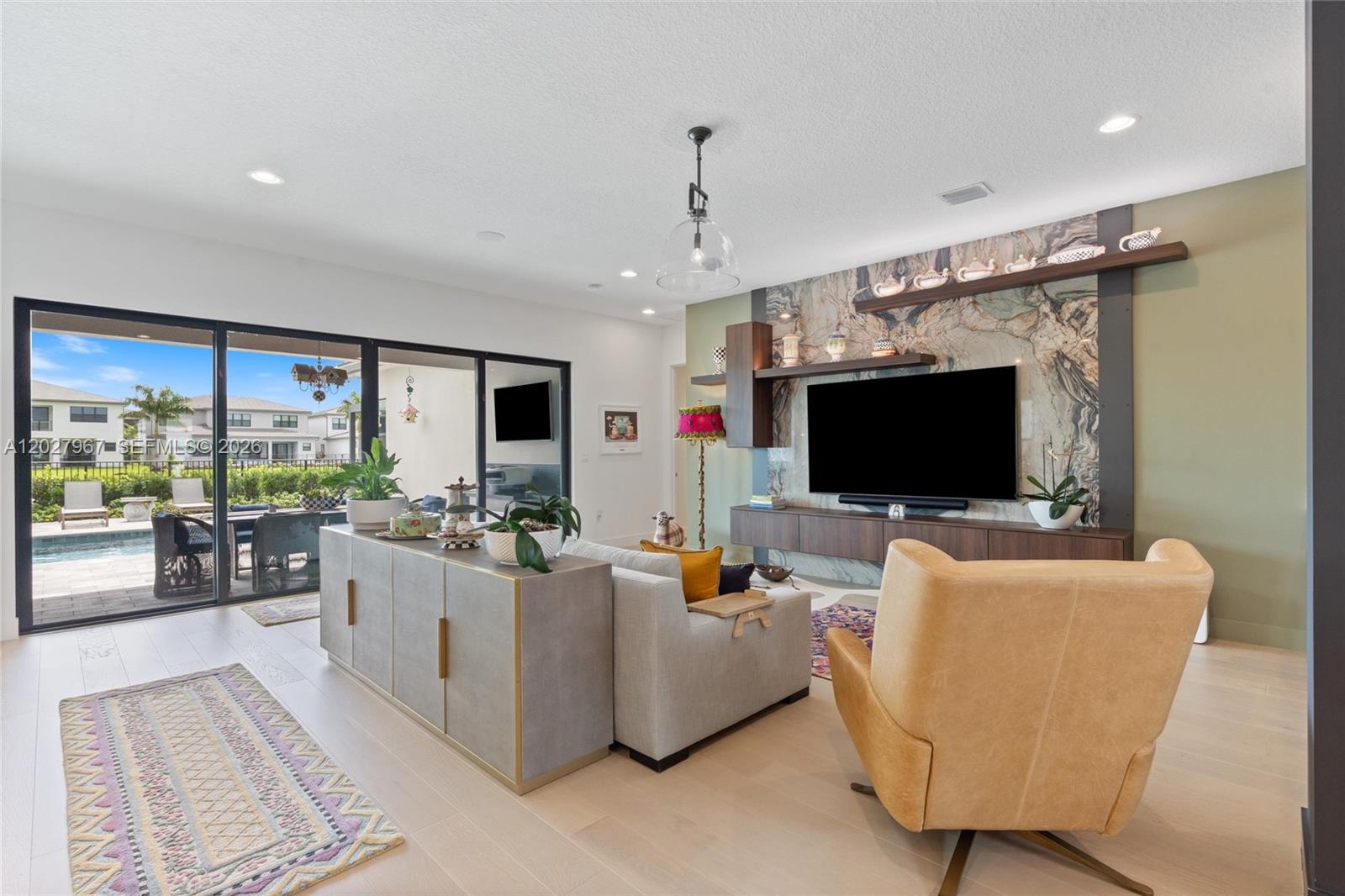 A living room features a stone accent wall, a television, and sliding doors to a patio — 20108 Castle Stuart Ave, Boca Raton FL 33434, BOCA RATON, FL
