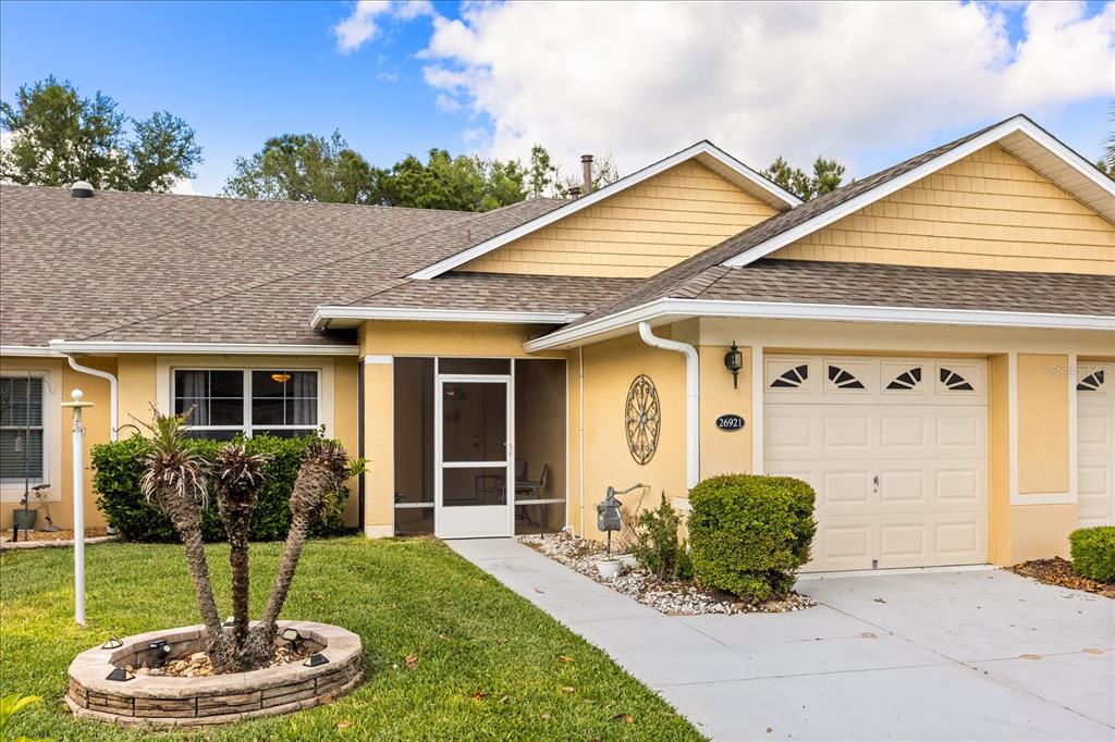 A yellow single-story house features a screened front porch, a garage, and a landscaped yard — 26921 WHITE PLAINS WAY, LEESBURG, FL