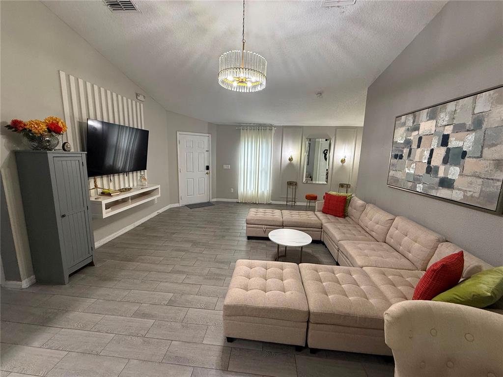 A living room features a large sectional sofa, a wall-mounted television, and tile flooring — 1875 ROYAL RIDGE DRIVE, DAVENPORT, FL