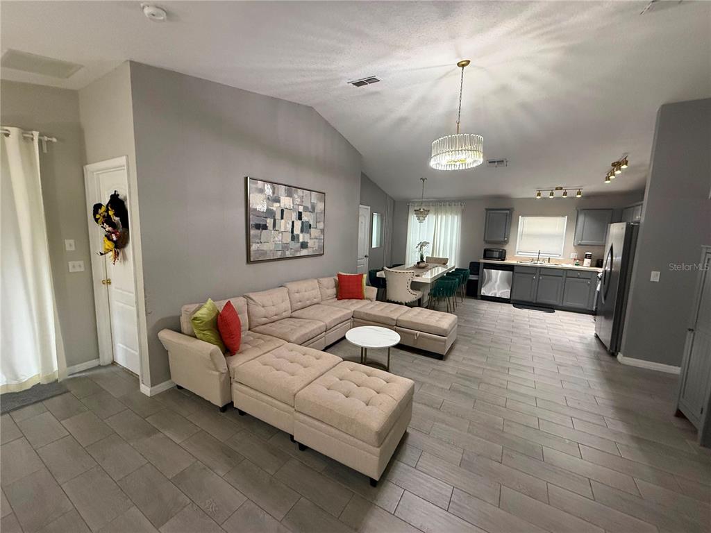 An open-concept living room and kitchen feature gray tile flooring, a sectional sofa, and vaulted ceilings — 1875 ROYAL RIDGE DRIVE, DAVENPORT, FL