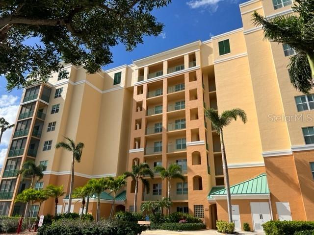 A multi-story tan apartment building features balconies and palm trees under a blue sky — 2090 MATECUMBE KEY ROAD UNIT 1105, PUNTA GORDA, FL