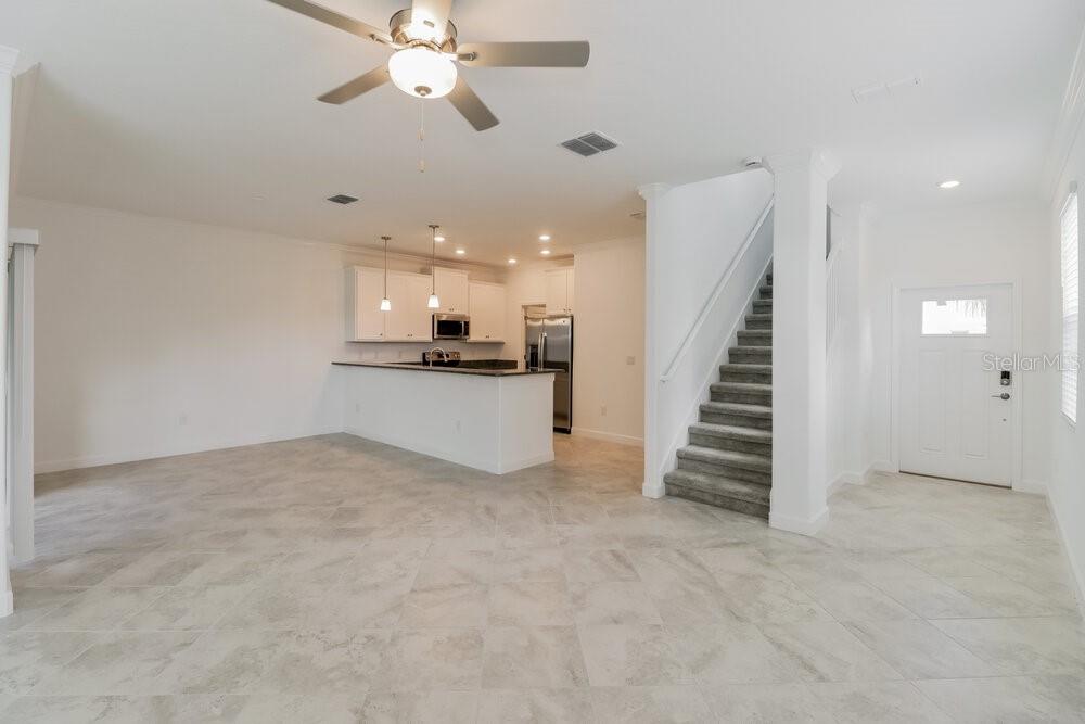 An open-concept living area features tile flooring, a kitchen with white cabinets, and carpeted stairs — 17506 RADIANT SHINE WAY, LUTZ, FL