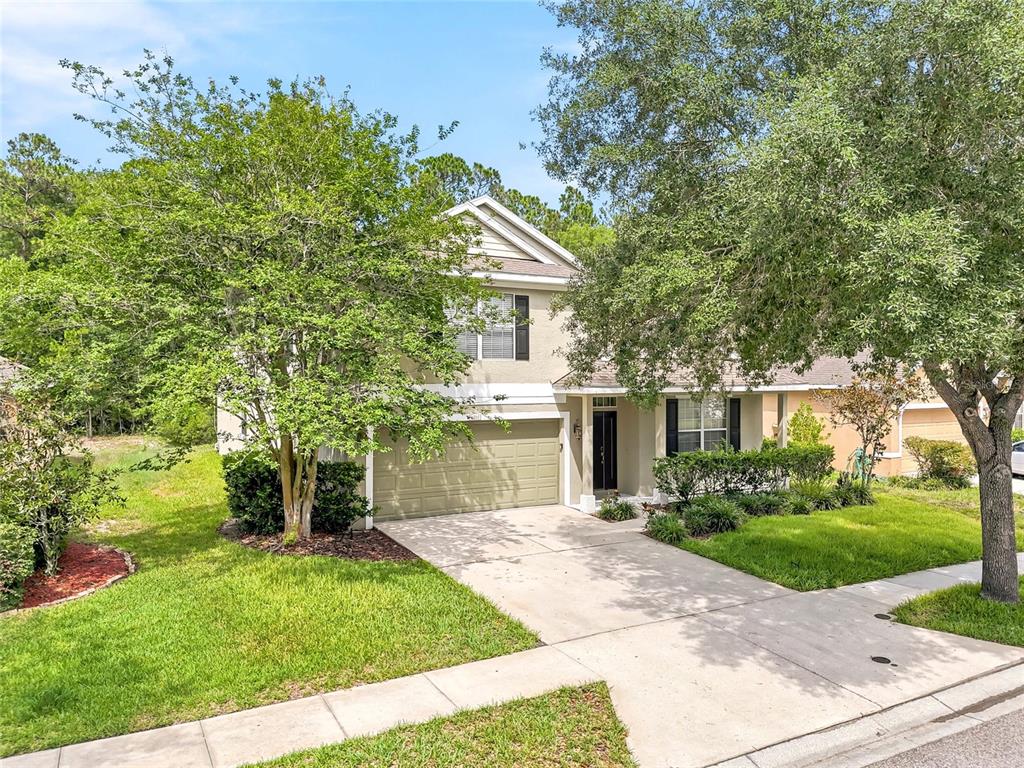 A two-story suburban house with a tan exterior, a two-car garage, and mature trees — 12230 COLONY LAKES BOULEVARD, NEW PORT RICHEY, FL