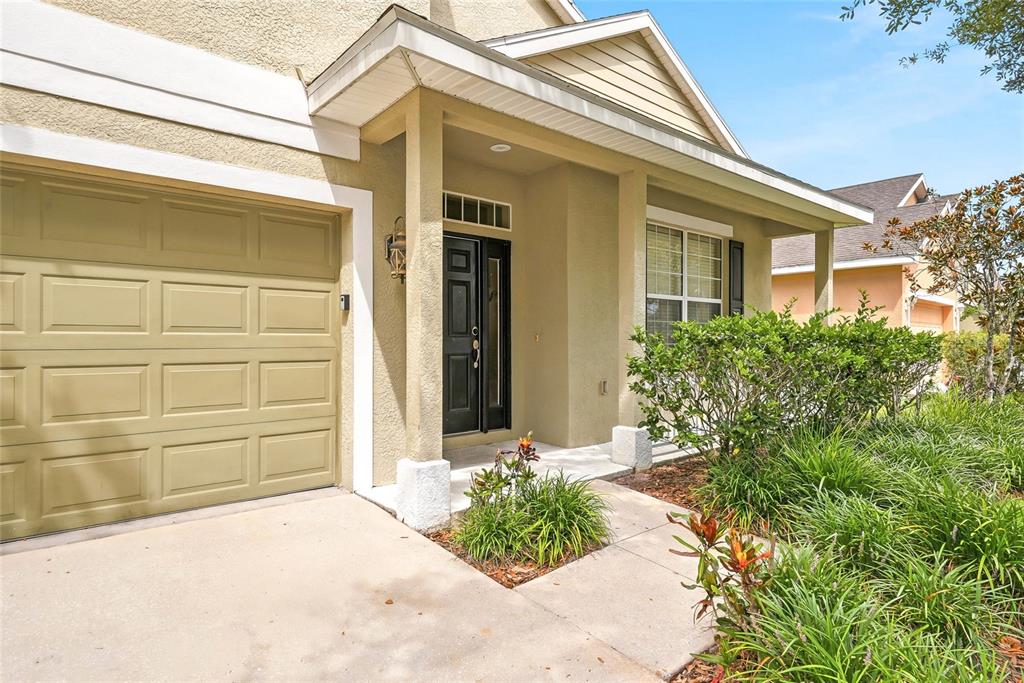 A tan house exterior features a single-car garage, a covered entryway, and a front garden — 12230 COLONY LAKES BOULEVARD, NEW PORT RICHEY, FL