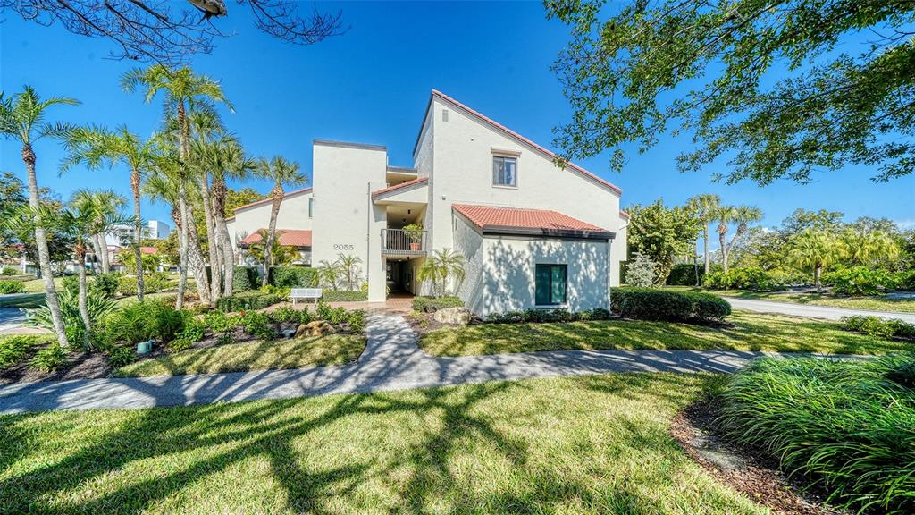 A two-story stucco apartment building with a tile roof and palm trees on a sunny day — 2055 GULF OF MEXICO DRIVE UNIT G2-109, LONGBOAT KEY, FL
