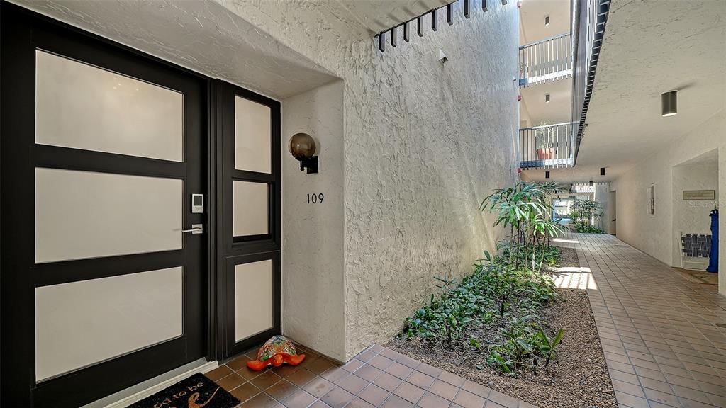 A modern front door with frosted glass panels sits beside a small landscaped garden area — 2055 GULF OF MEXICO DRIVE UNIT G2-109, LONGBOAT KEY, FL