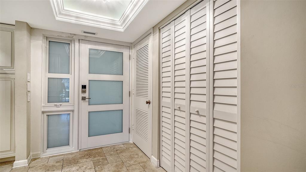 An entryway features a white door with frosted glass panels, tiled flooring, and louvered closet doors — 2055 GULF OF MEXICO DRIVE UNIT G2-109, LONGBOAT KEY, FL