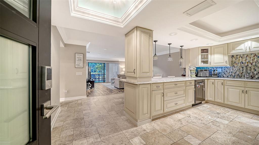 A kitchen with cream-colored cabinets and stone tile flooring opens into a living area — 2055 GULF OF MEXICO DRIVE UNIT G2-109, LONGBOAT KEY, FL