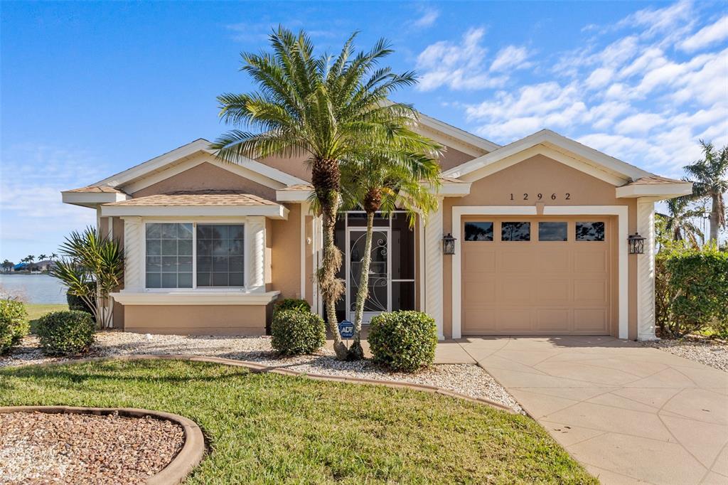 A single-story house with a tan exterior, a two-car garage, and a palm tree out front — 12962 SW DOUG DRIVE, LAKE SUZY, FL