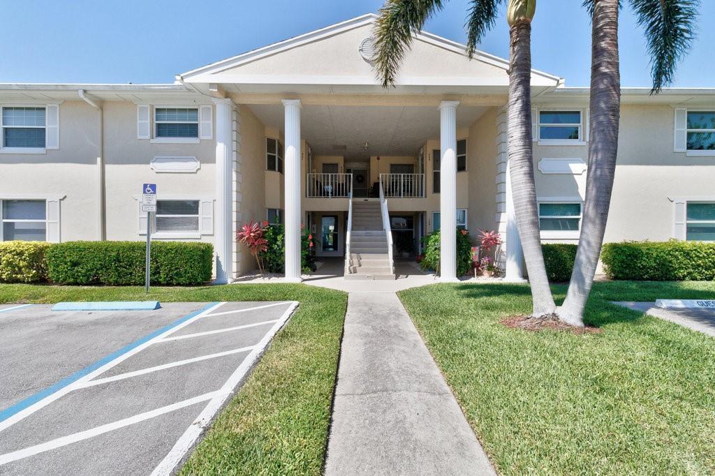 A two-story apartment building exterior features a central staircase, white columns, and palm trees — VERO BEACH, FL