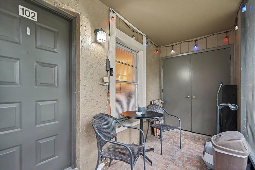 A small covered patio features a bistro set, a storage closet, and string lights — 14203 SHADOW MOSS LANE UNIT 102, TAMPA, FL