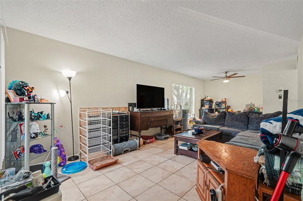 A living room with tile flooring, a dark sofa, a television, and a display shelf — 14203 SHADOW MOSS LANE UNIT 102, TAMPA, FL