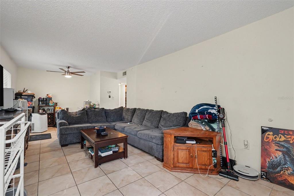A living room features a large gray sectional sofa, a coffee table, and tile flooring — 14203 SHADOW MOSS LANE UNIT 102, TAMPA, FL