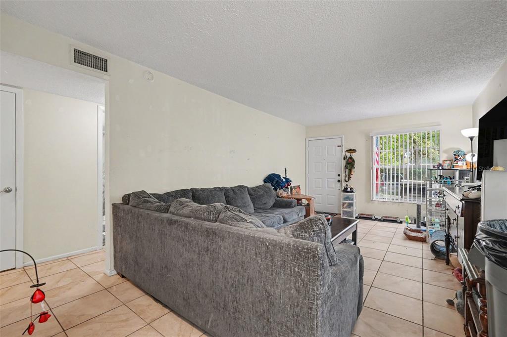 A living room features a gray sectional sofa, tile flooring, and a front entry door — 14203 SHADOW MOSS LANE UNIT 102, TAMPA, FL