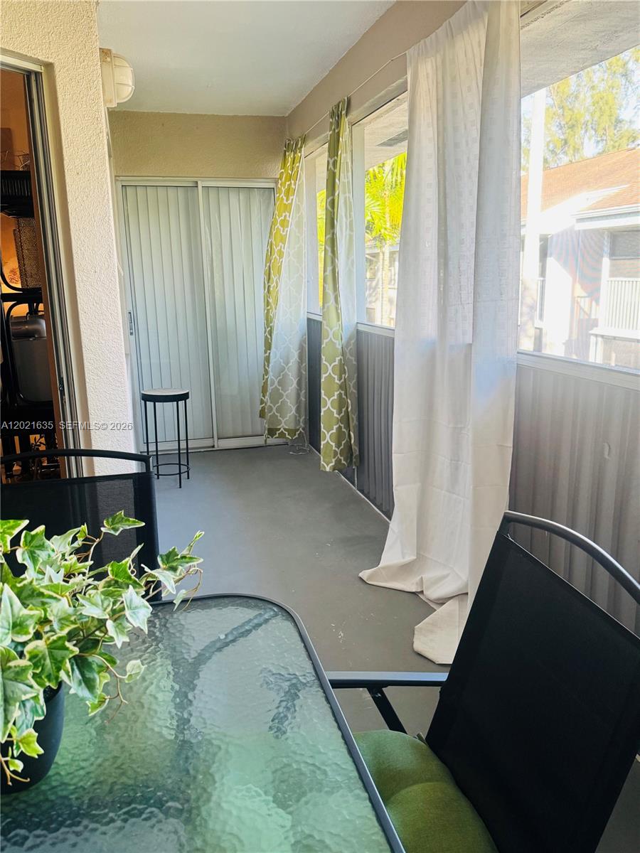 A covered balcony features a glass-topped table, chairs, patterned curtains, and sliding glass doors — 2638 SE 21st Ct # C, Homestead FL 33035, HOMESTEAD, FL
