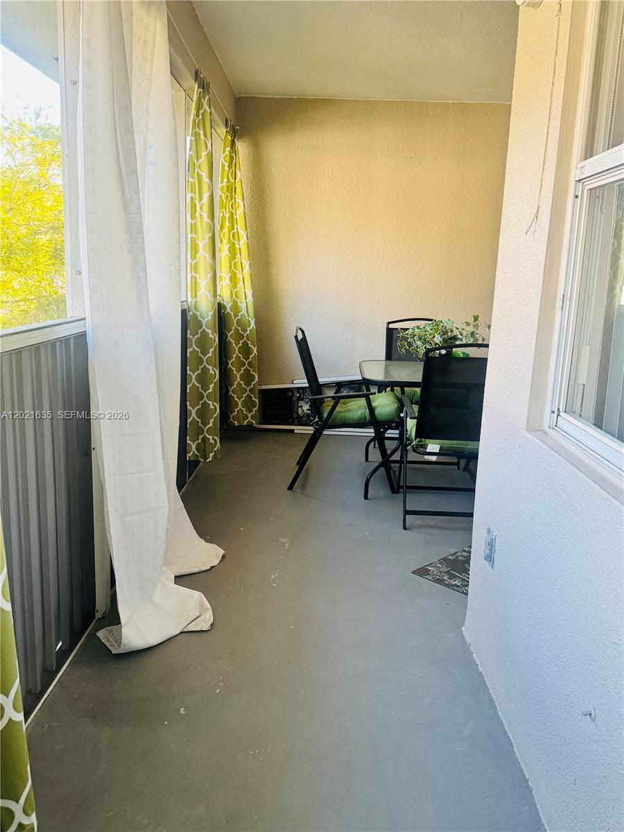 A covered balcony features a small dining set, green patterned curtains, and gray flooring — 2638 SE 21st Ct # C, Homestead FL 33035, HOMESTEAD, FL