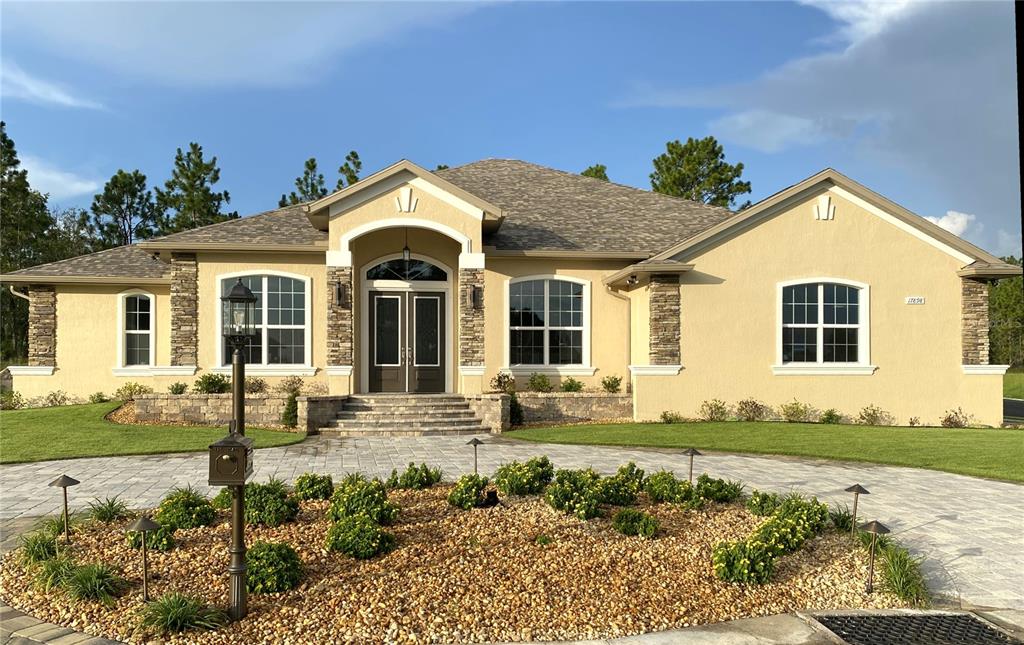 A single-story house with a beige stucco exterior, stone accents, and a paved circular driveway — 17898 SW 72ND STREET ROAD, DUNNELLON, FL