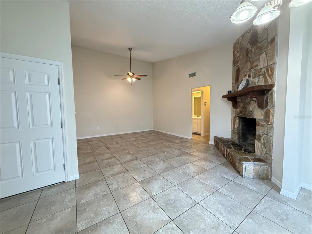 A living room features tile flooring, a stone fireplace, and a vaulted ceiling with a fan — 3136 JULIA COURT, LAKELAND, FL