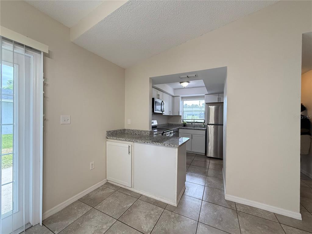A kitchen with granite countertops and stainless steel appliances opens to a tiled dining area — 3136 JULIA COURT, LAKELAND, FL