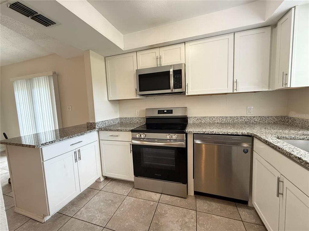 A kitchen features white cabinets, granite countertops, stainless steel appliances, and tiled flooring — 3136 JULIA COURT, LAKELAND, FL