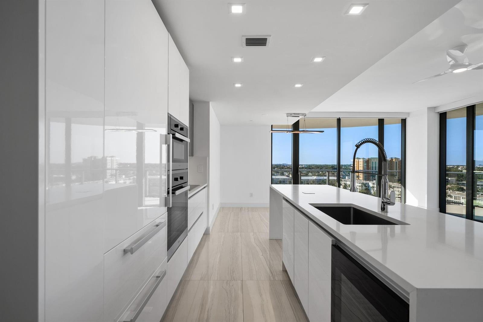 A modern kitchen features white glossy cabinets, a large island with a sink, and floor-to-ceiling windows — 730 N Ocean Boulevard # 801, Pompano Beach FL 33062, POMPANO BEACH, FL