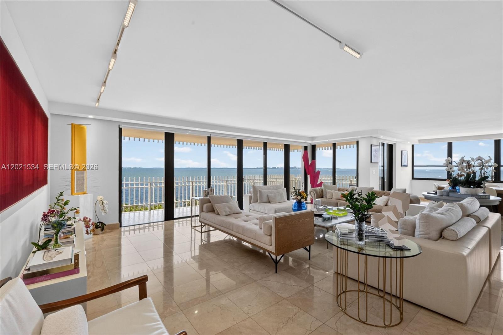 A bright living room features marble floors, neutral furniture, and floor-to-ceiling windows overlooking the ocean — 2 Grove Isle Dr # 802, Miami FL 33133, MIAMI, FL