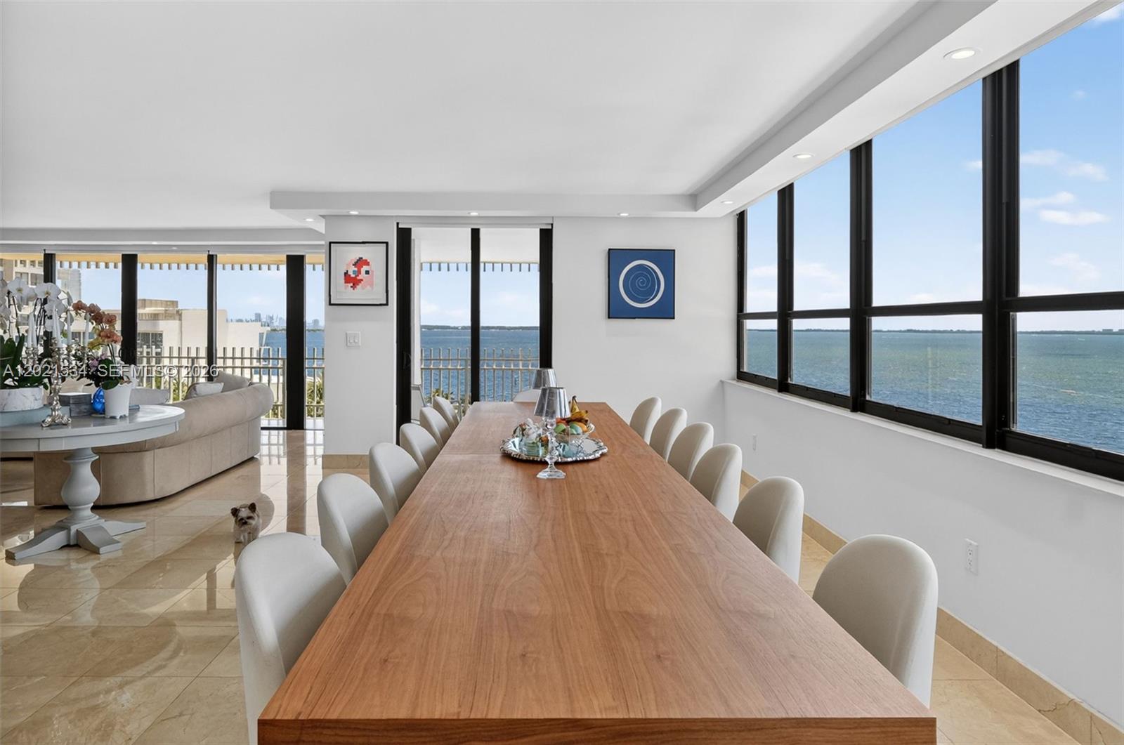 A long wooden dining table sits in a bright room with floor-to-ceiling ocean views — 2 Grove Isle Dr # 802, Miami FL 33133, MIAMI, FL