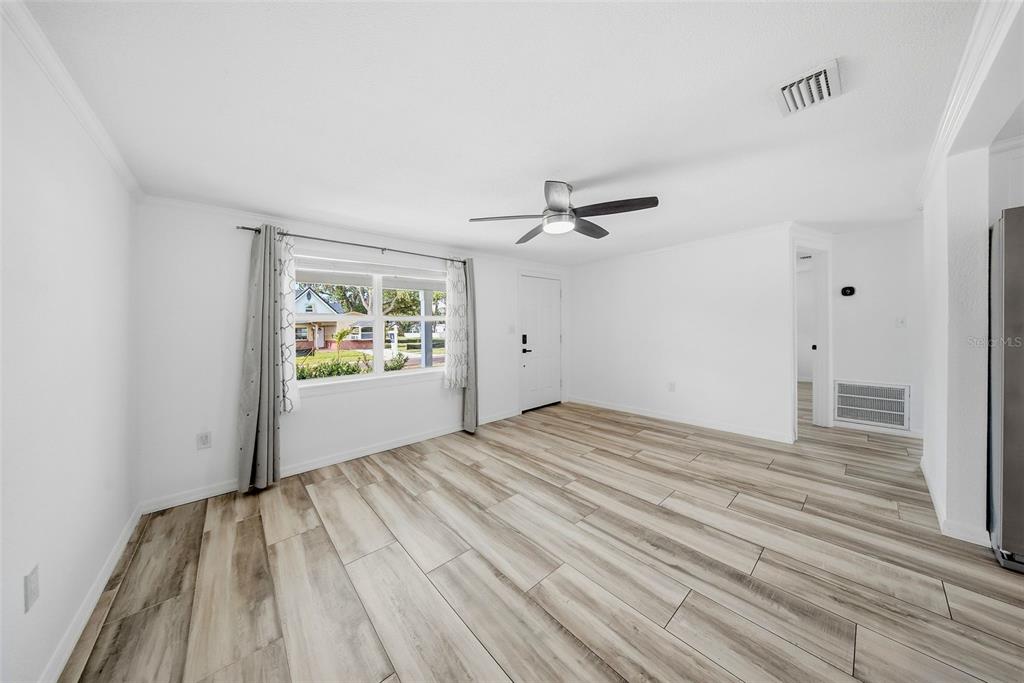 A bright, empty living room features white walls, light wood-look flooring, and a ceiling fan — 1565 CONNECTICUT AVENUE NE, ST PETERSBURG, FL