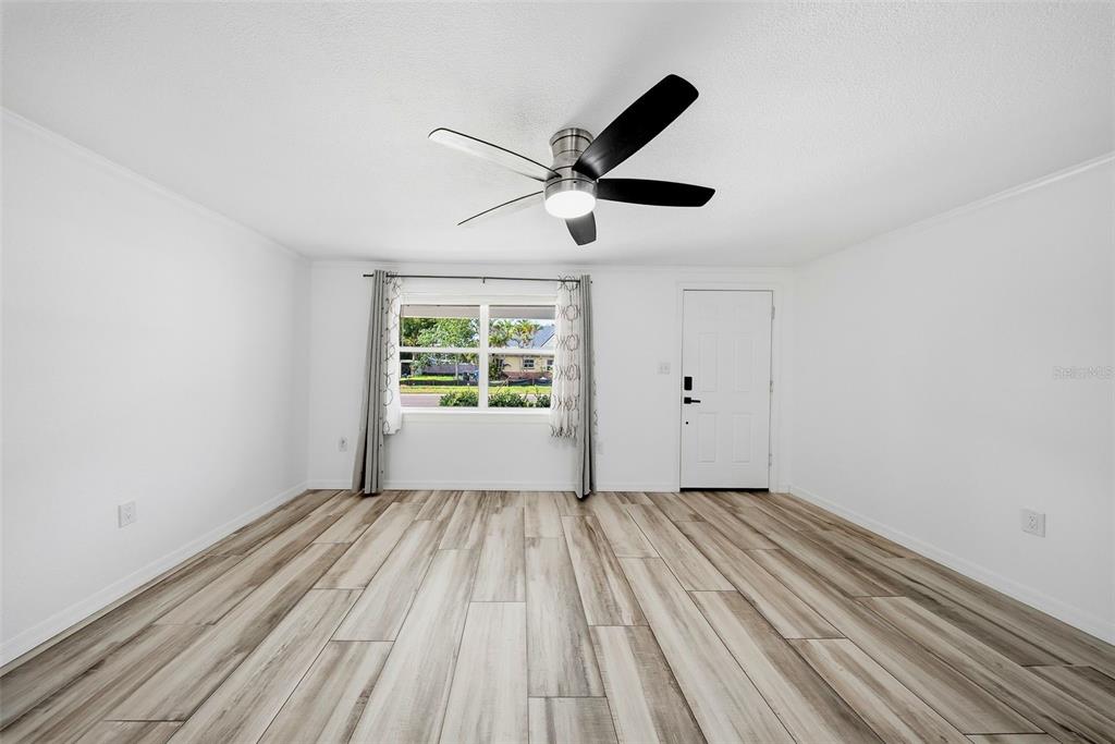 A bright, empty room features white walls, wood-look flooring, a ceiling fan, and a window — 1565 CONNECTICUT AVENUE NE, ST PETERSBURG, FL