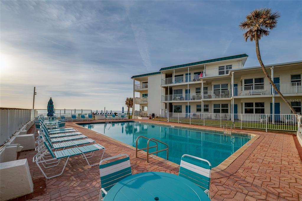 A swimming pool sits on a brick patio in front of a multi-story beachside building — 935 S ATLANTIC AVENUE UNIT 165, DAYTONA BEACH, FL