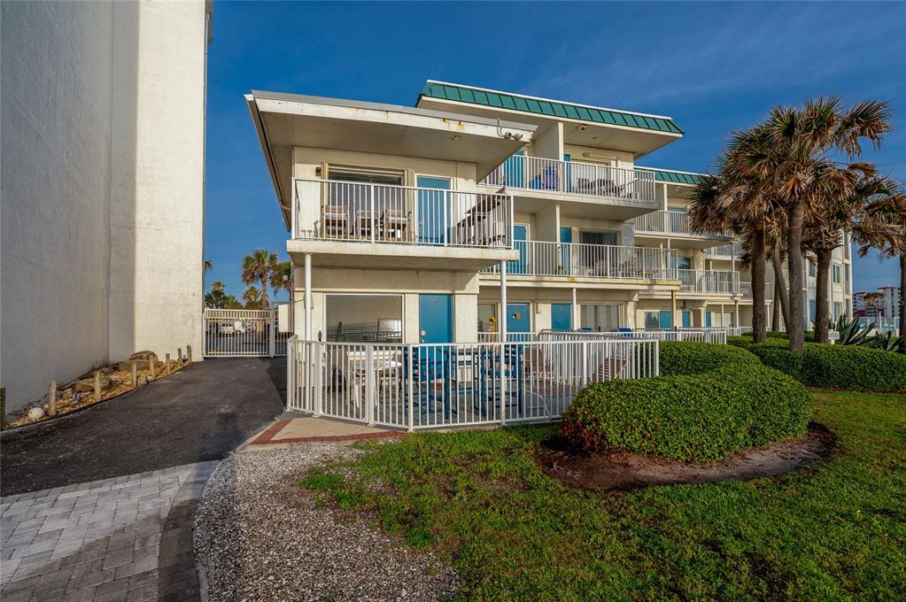 A two-story coastal building features white balconies, blue doors, and a fenced-in patio area — 935 S ATLANTIC AVENUE UNIT 165, DAYTONA BEACH, FL