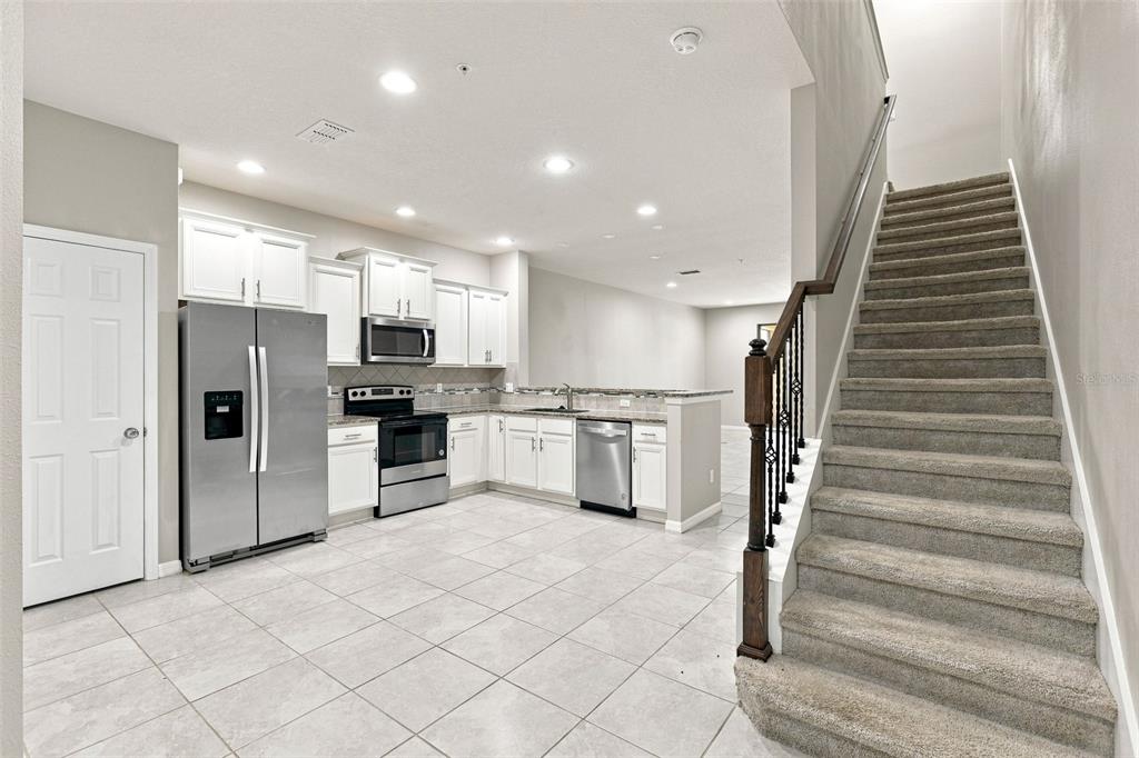 A kitchen with white cabinets, stainless steel appliances, and tile flooring next to a staircase — 1236 PAVIA DRIVE, APOPKA, FL