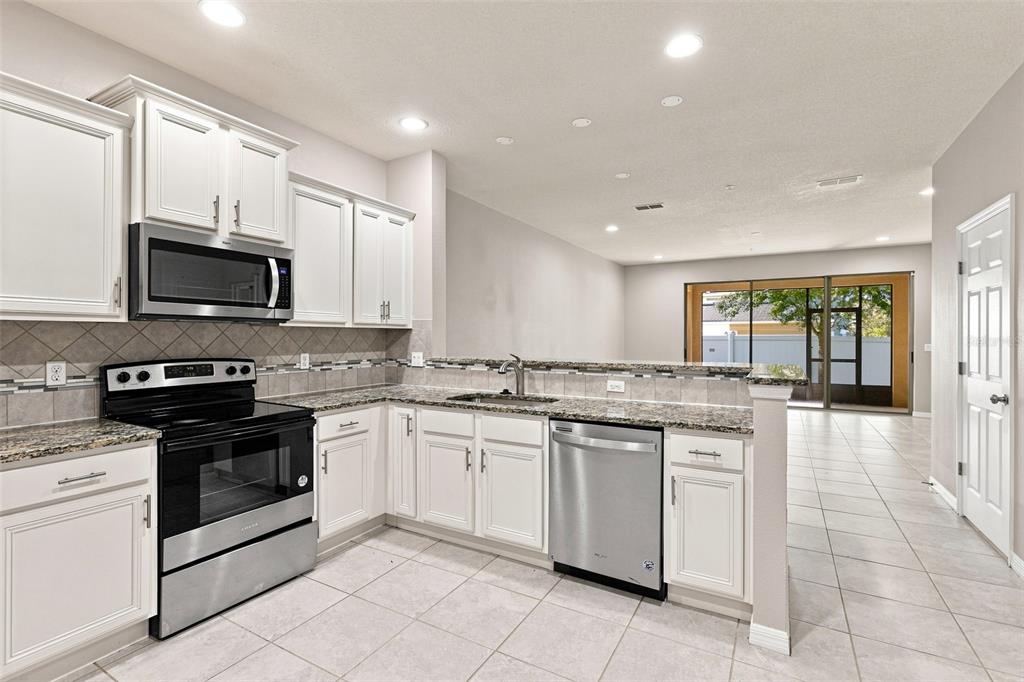 A kitchen with white cabinets, granite countertops, stainless steel appliances, and tile flooring — 1236 PAVIA DRIVE, APOPKA, FL