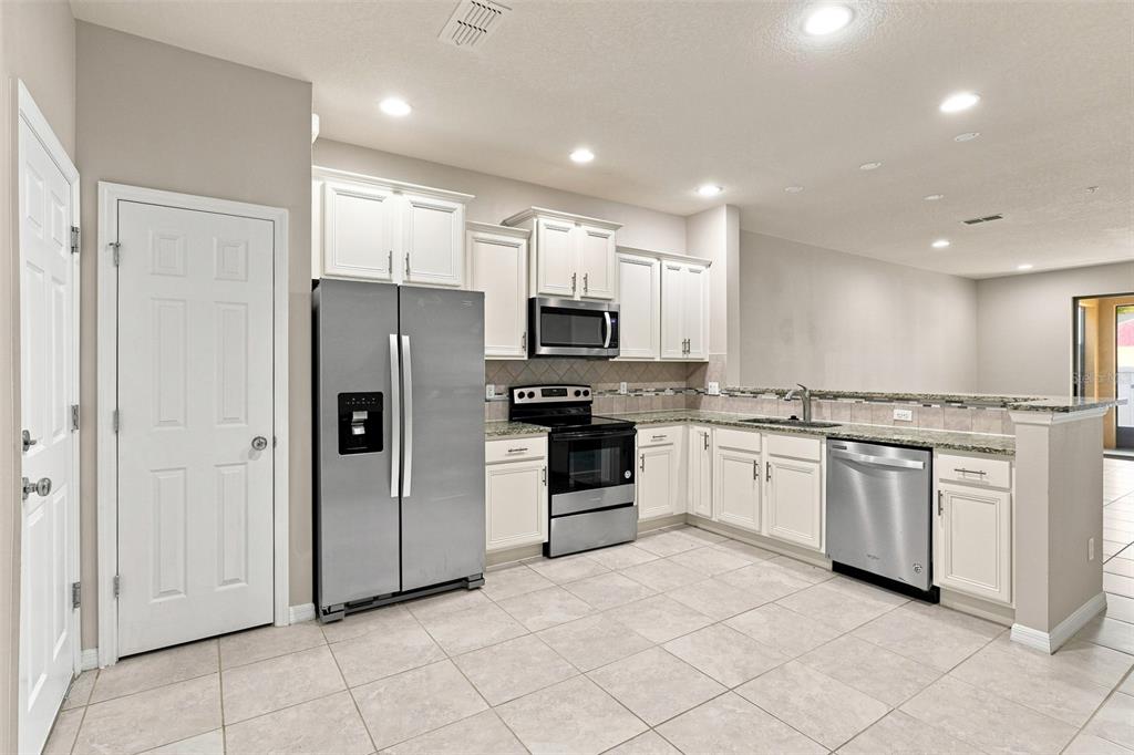 A kitchen features white cabinets, stainless steel appliances, granite countertops, and light-colored tile flooring — 1236 PAVIA DRIVE, APOPKA, FL