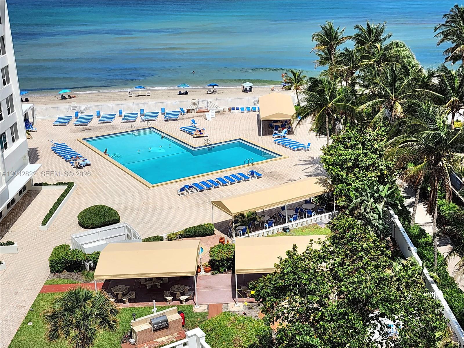 An aerial view shows a swimming pool, lounge chairs, and cabanas near a sandy beach — 3505 S Ocean Dr # 821, Hollywood FL 33019, HOLLYWOOD, FL
