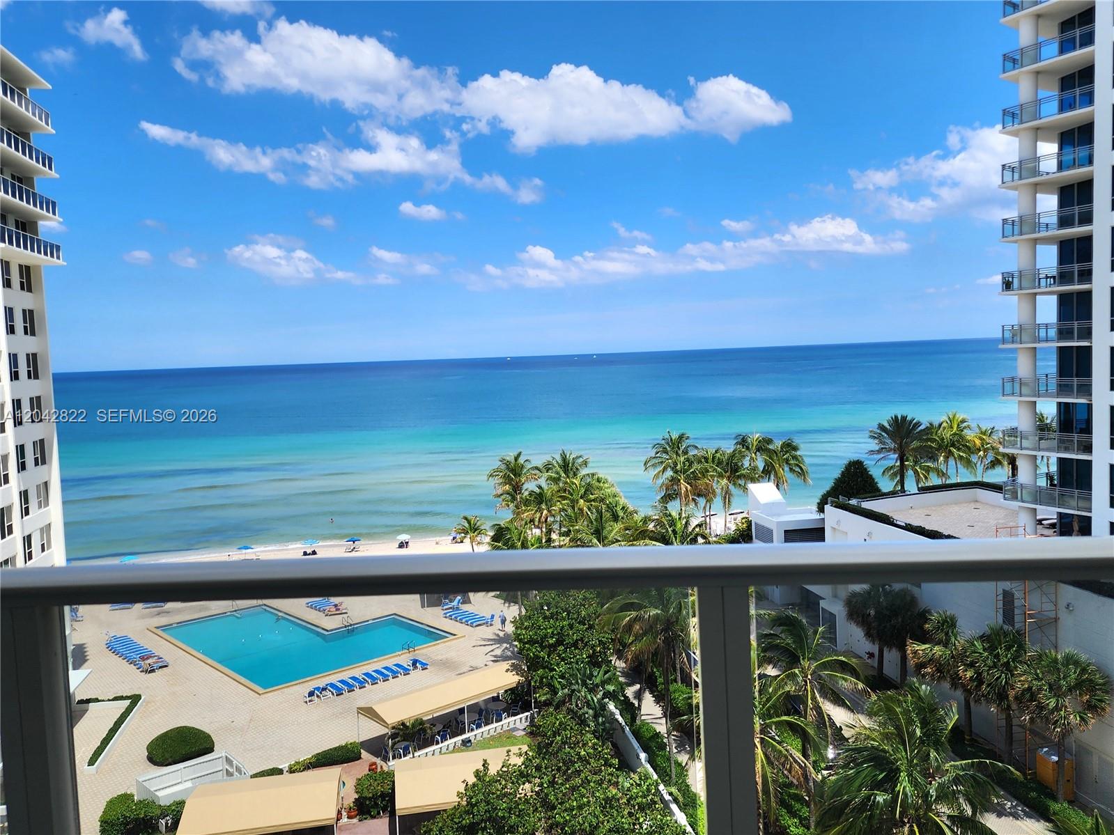 A balcony view overlooks a swimming pool, palm trees, and the ocean between two buildings — 3505 S Ocean Dr # 821, Hollywood FL 33019, HOLLYWOOD, FL