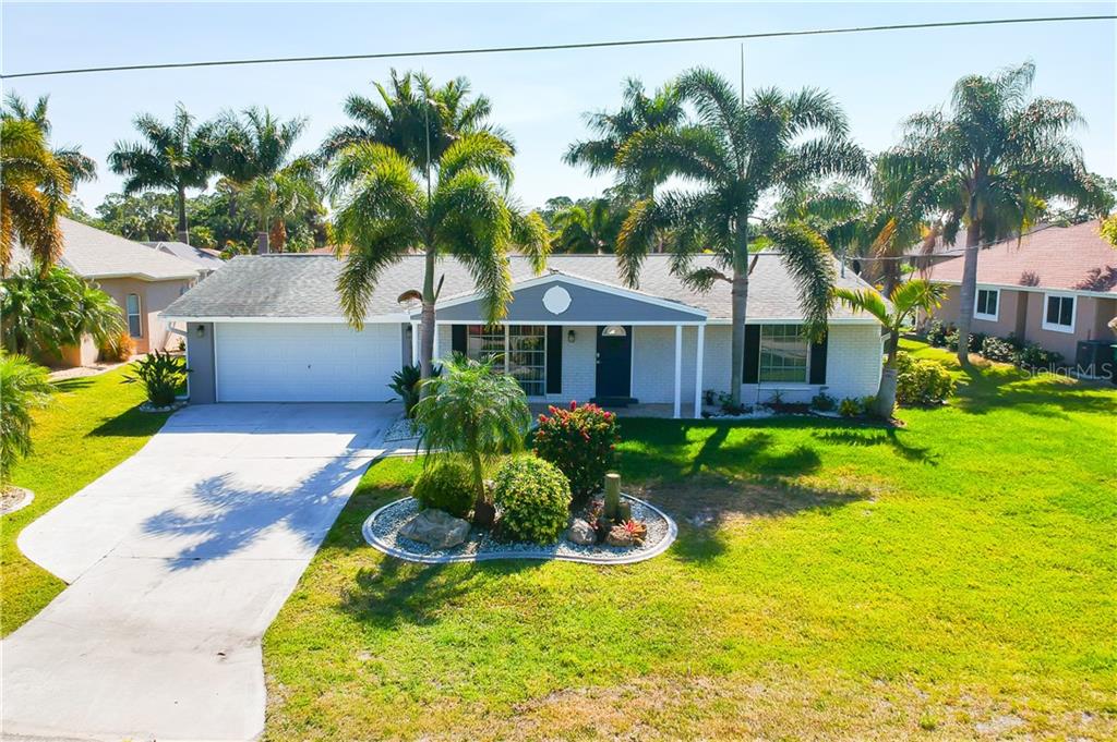 A single-story house with a white brick exterior, a two-car garage, and several palm trees — 18289 WOLBRETTE CIRCLE, PORT CHARLOTTE, FL